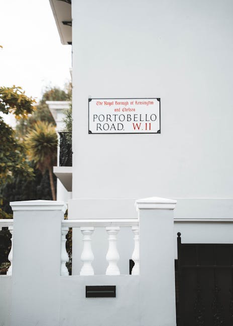 A close-up of a white residential building on Portobello Road, Notting Hill W11, showing a decorative balcony with classical balusters and a black mailbox inset into the wall. The exterior wall is cle